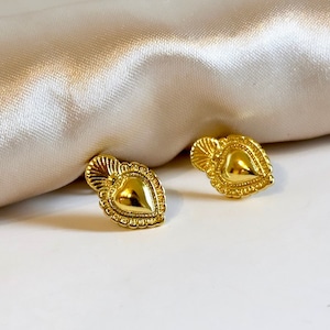 Peut inclure: Une paire de boucles d'oreilles en forme de cœur dorées avec des détails complexes. Les boucles d'oreilles ont un motif de cœur en relief avec une bordure texturée.
