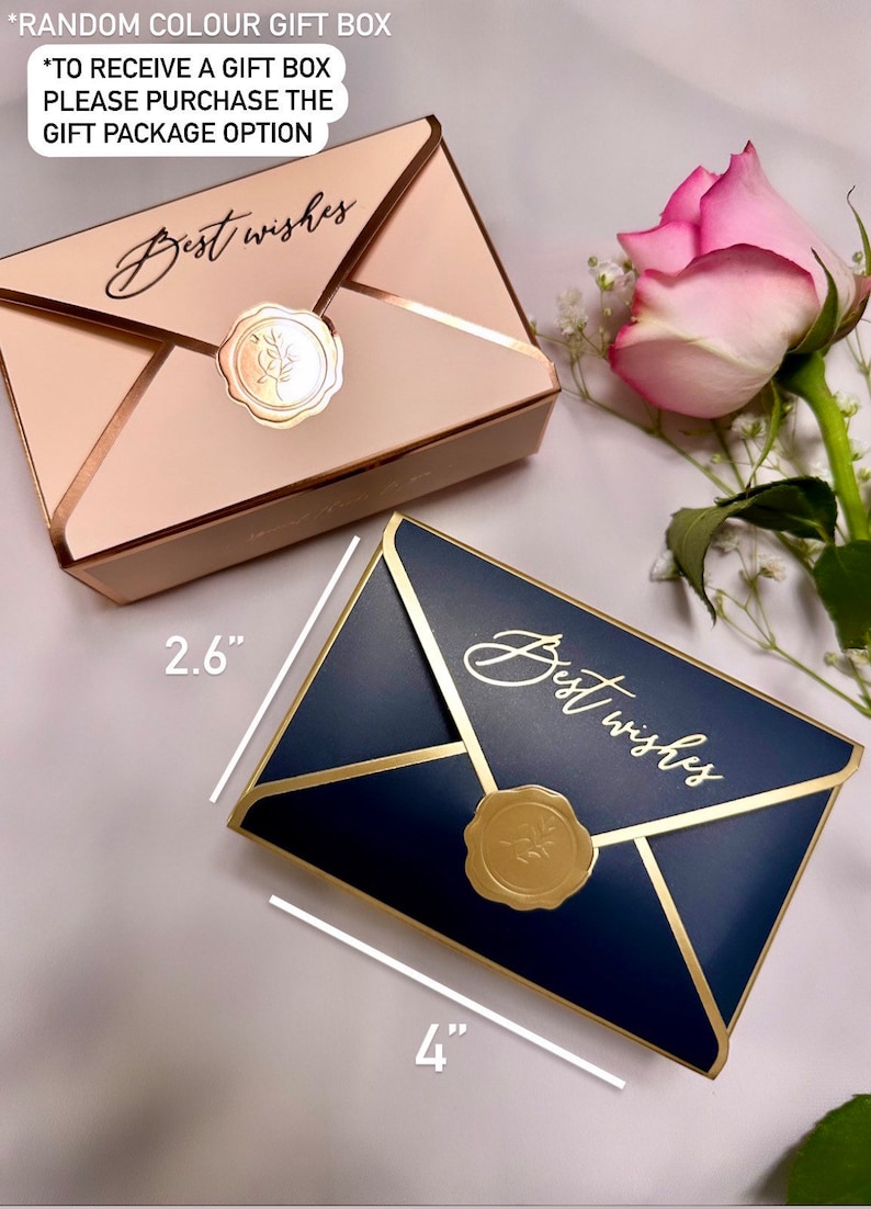 May include: Two envelope-shaped gift boxes, one beige and one navy blue, with gold accents and a gold seal that reads "Best wishes." The navy box measures 4 inches long. A pink rose and baby's breath are in the background.