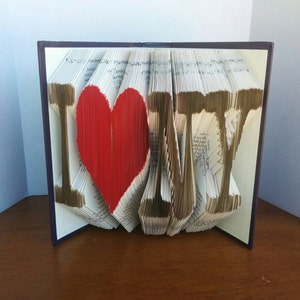May include: A book art sculpture of the words "I love NY" with a red heart in place of the "O". The sculpture is made from the pages of a book that have been folded and shaped into letters.
