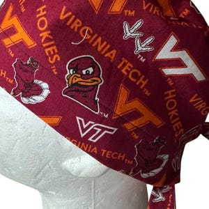 May include: Maroon and orange Virginia Tech Hokies patterned head covering. The fabric features the Virginia Tech logo, the words "Virginia Tech" and "Hokies", and the VT logo. The head covering is tied at the back.
