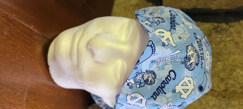 May include: A blue and white patterned surgical scrub hat with the text "Carolina" and "Tar Heels" repeated throughout the design.