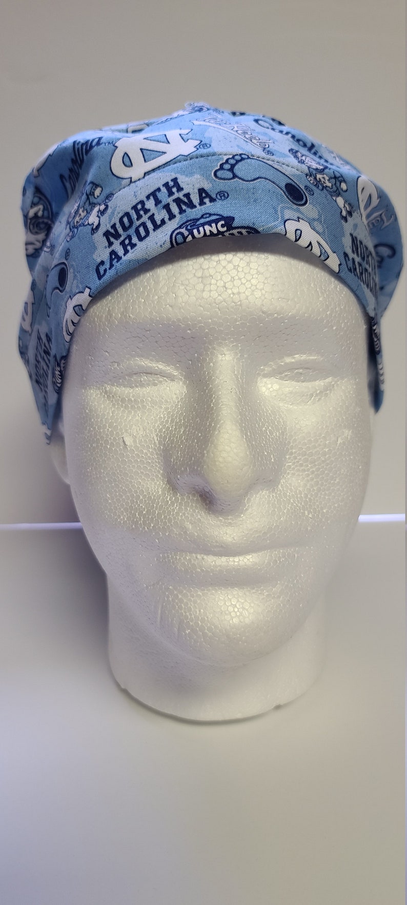 May include: A light blue scrub hat with a white and blue pattern featuring the words "North Carolina" and "UNC".