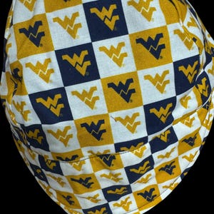 May include: A patterned hat featuring a repeating checkerboard design of gold, navy blue, and white squares. Each square contains the stylized logo of the West Virginia Mountaineers. The hat is made of fabric and has a rounded shape.