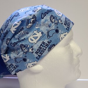May include: Blue and white surgical scrub hat with a North Carolina Tar Heels pattern. The hat has a blue ribbon tied at the back.