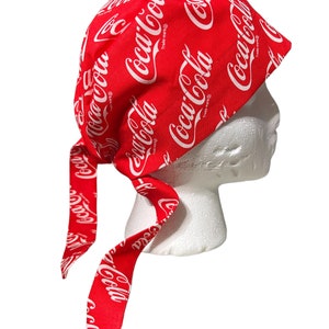 May include: Red and white patterned bandana with the Coca-Cola logo repeated throughout. The bandana is tied around a white mannequin head.