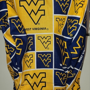 May include: A yellow and blue fabric scrub hat with a repeating pattern of the West Virginia University logo. The hat has a tie on the back.