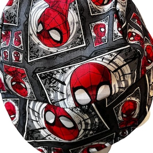 May include: A black and gray patterned hat featuring a repeating design of the superhero Spider-Man's face in red. The hat's fabric has a textured appearance, with the Spider-Man images framed in white.