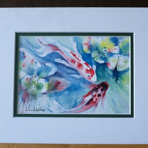 May include: Watercolor painting of three koi fish swimming in a pond with lily pads. The fish are red, white, and black with spots. The lily pads are green and yellow.