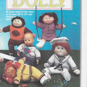 May include: A book cover with the title "Knit It For Dolly" and a photo of five Cabbage Patch Kids dolls wearing knitted clothing. The dolls are 40 to 48 cm tall and are dressed in a variety of outfits, including a sailor suit, a sweater with a diamond pattern, a football jersey, and a yellow jacket. The book cover also includes the text "10 super knits in two sizes to fit your 40 cm to 48 cm soft-sculpture dolls."