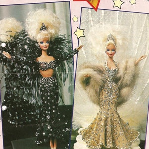 May include: Two Barbie dolls dressed in glamorous gowns. One doll wears a black gown with feathers and rhinestones, the other wears a gold gown with fur and rhinestones. The dolls are posed on a white background with stars.