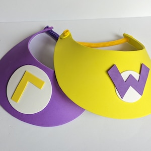 May include: Two foam visors, one purple and one yellow. The purple visor has a white circle with a yellow L-shaped design. The yellow visor has a white circle with a purple W design. Both visors have a flexible band for the head.