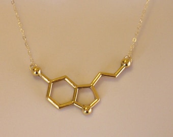 May include: A gold necklace with a pendant shaped like the chemical structure of serotonin.