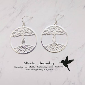May include: Silver earrings with a tree of life design featuring a DNA strand in the trunk. The earrings are circular and have a delicate, intricate design. Nikola Jewelry: Beauty in Math, Science, and Nature. www.nikolajewelry.etsy.com