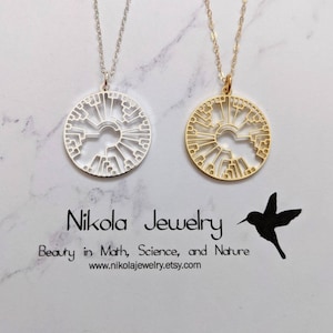 May include: Two necklaces with a circular pendant featuring a tree of life design. One necklace has a silver pendant and chain, the other has a gold pendant and chain. The necklaces are on a white marble surface with the text "Nikola Jewelry" and "Beauty in Math, Science, and Nature" below the necklaces.