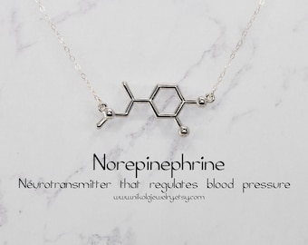 Könnte beinhalten: Silberne Halskette mit einem chemischen Struktur-Anhänger, der Noradrenalin darstellt, einen Neurotransmitter, der den Blutdruck reguliert. Der Anhänger befindet sich an einer silbernen Kette. Der Text "Noradrenalin" und "Neurotransmitter, der den Blutdruck reguliert" befindet sich unter dem Anhänger. Der Text "www.unikaljewelry.etsy.com" befindet sich unter dem Text.