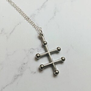 May include: A silver necklace with a geometric pendant featuring a cross shape with five round balls at the ends of each arm.