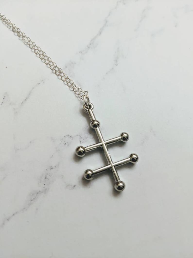 May include: A silver necklace with a geometric pendant featuring a cross shape with five round balls at the ends of each arm.