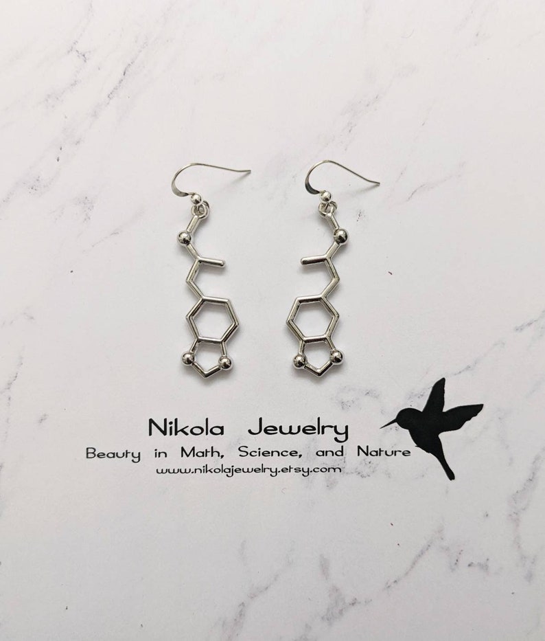 May include: Silver earrings shaped like a chemical structure, with a small ball at the end of each chain. The earrings are hanging from a white background with the text "Nikola Jewelry Beauty in Math, Science, and Nature www.nikolajewelry.etsy.com".