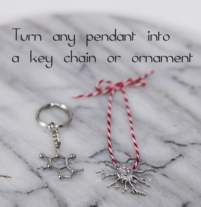May include: Two silver pendants, one shaped like a molecule and the other like a snowflake, are shown on a white marble surface. One pendant is attached to a silver key chain and the other is attached to a red and white string.