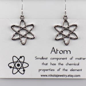 May include: Silver atom earrings with a simple design. The earrings are on a white card with the text "Atom, Smallest component of matter that has the chemical properties of the element www.nikolajewelry.etsy.com".