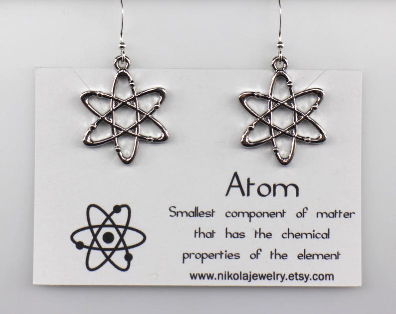 May include: Silver atom earrings with a simple design. The earrings are on a white card with the text "Atom, Smallest component of matter that has the chemical properties of the element www.nikolajewelry.etsy.com".