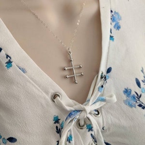 May include: A silver necklace with a geometric cross pendant. The cross is made of small silver balls connected by thin silver bars.