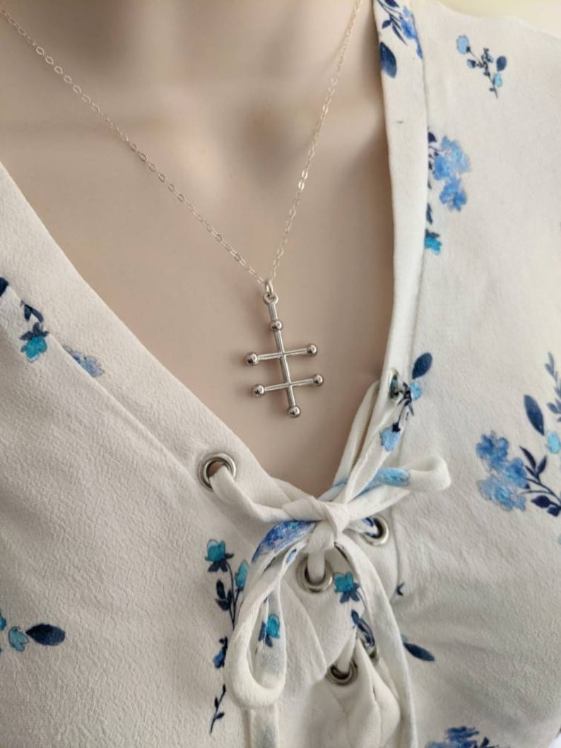 May include: A silver necklace with a geometric cross pendant. The cross is made of small silver balls connected by thin silver bars.