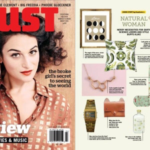 May include: A magazine cover featuring a woman with dark hair and a red lip. The magazine is titled "Bust" and the cover story is "The broke girl's secret to seeing the world". The cover also features the text "Fall Preview" and "The Best TV, Movies & Music". The right side of the image shows a spread of products with a natural theme, including a t-shirt with a print of rocks and minerals, a pillow with a botanical print, a necklace with a chemical structure pendant, a watch with a wooden band, a leather wallet, and a bottle of liquid.