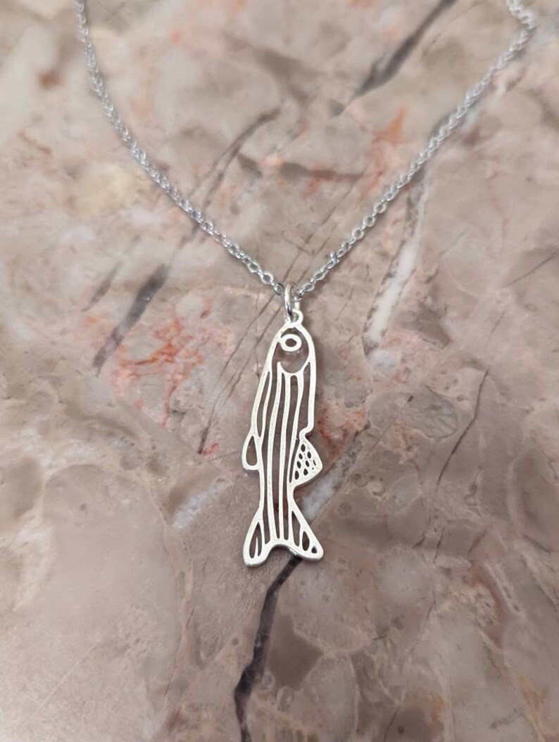 May include: A silver necklace featuring a delicate fish pendant. The fish is outlined and has a detailed design.