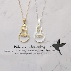 May include: Two light bulb necklaces, one gold and one silver, on a white marble background. The necklaces feature a simple, minimalist light bulb design. The text "Nikola Jewelry" is visible at the bottom of the image.