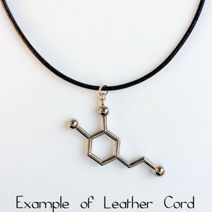 May include: A silver necklace with a pendant shaped like a chemical molecule. The necklace is on a black leather cord. "Example of Leather Cord" is written below the necklace.