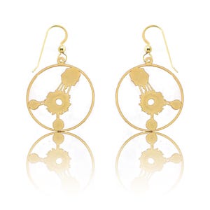 May include: Gold-toned earrings with a circular design featuring a stylized image of a cell. The earrings have a simple hook closure.