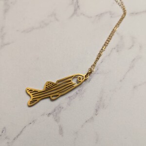 May include: A gold chain necklace featuring a delicate fish pendant. The fish is outlined in a simple, minimalist style.