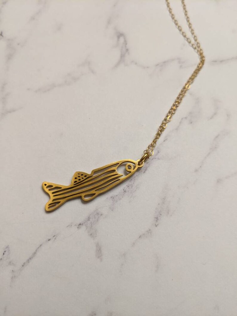 May include: A gold chain necklace featuring a delicate fish pendant. The fish is outlined in a simple, minimalist style.