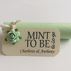 May include: A mint green favour box with a white tag that says "Mint to be" with the date "19-07-06" and the names "Charlotte & Anthony". The tag is decorated with a small green flower.
