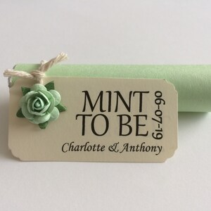 May include: A mint green and white wedding favour with a tag that reads "Mint to Be" with the date "19-07-09" and the names "Charlotte & Anthony".