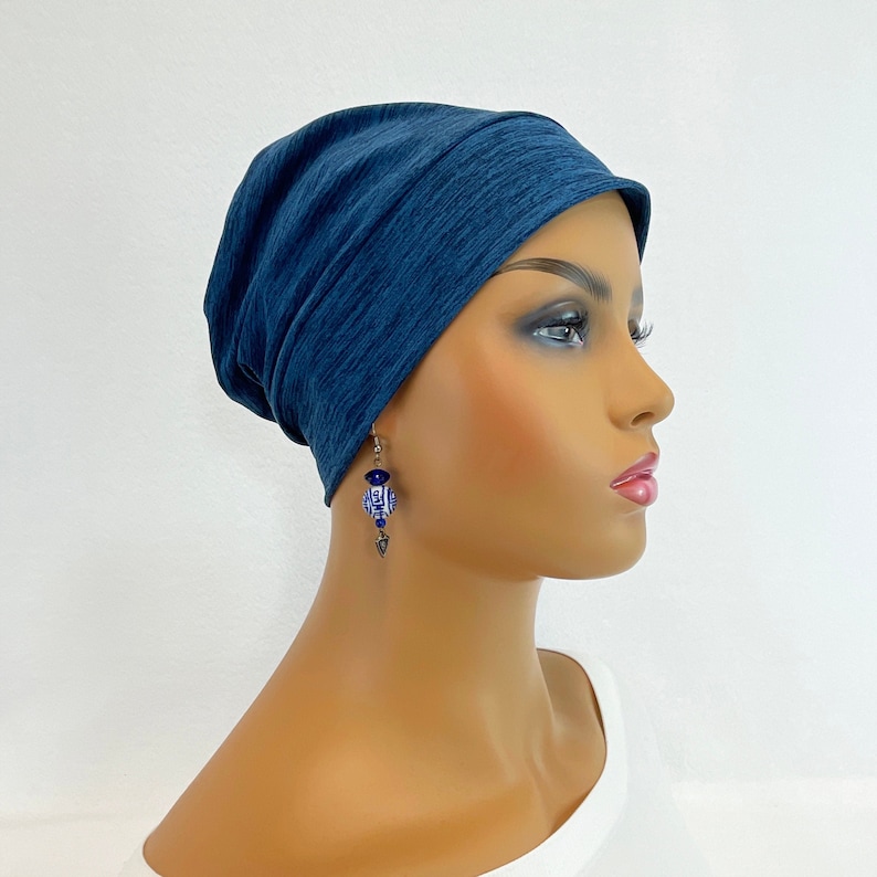 May include: A dark blue beanie-style hat and a pair of earrings. The earrings feature blue and white decorative beads with silver-colored metal accents. The hat is made of a soft, textured fabric.