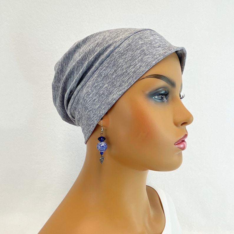 Puede incluir: Un gorro de punto gris y blanco jaspeado con un ajuste holgado. El gorro se lleva en un maniqu&iacute; con pendientes azules y blancos.