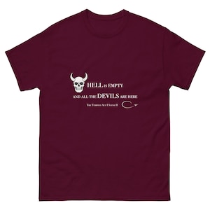 Puede incluir: Camiseta granate con un diseño de calavera blanca con cuernos y la frase "HELL IS EMPTY AND ALL THE DEVILS ARE HERE", una cita de La Tempestad. El texto está en una fuente clara y legible.