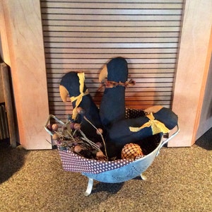 May include: Three black fabric birds with yellow ribbon accents are arranged in a silver colander with brown twigs and acorns. The colander is sitting on a brown carpet.