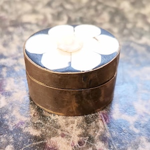 Peut inclure: Petite boîte ronde et antique avec un motif floral sur le couvercle. Le couvercle présente une fleur blanche sur un fond bleu foncé. La boîte a une bande métallique de couleur bronze sur les côtés.