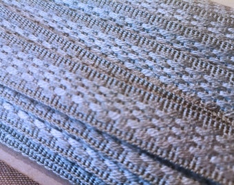 May include: Close-up of a stack of gray and white braided trim. The trim has a woven pattern and is made of a soft, textured material.