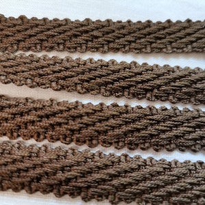 May include: Close-up of brown woven trim with a textured pattern. The trim is folded in four layers, showing the detail of the weave.