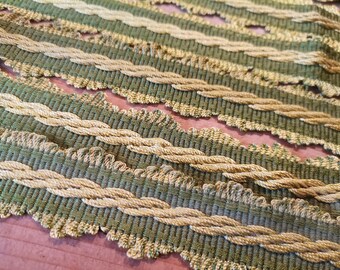 May include: Close-up of decorative trim with a repeating pattern. The trim features alternating bands of olive green woven fabric and twisted gold-coloured rope. The edges have a scalloped design. The trim is likely used for upholstery or craft projects.