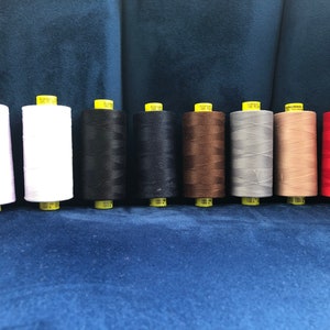 May include: Ten spools of thread in various colors, including white, black, brown, gray, and red. The spools are arranged in a row on a blue surface.