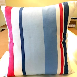 May include: A white pillow with blue, red, and pink stripes. The pillow is made of a soft, textured fabric.