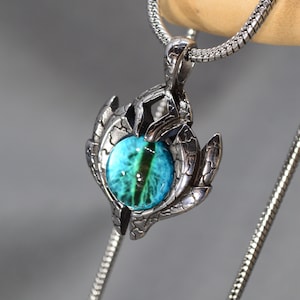 May include: A silver chain necklace with a pendant featuring a blue eye surrounded by a silver claw design.