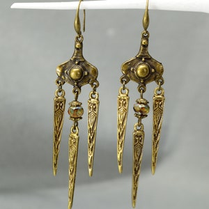 May include: A pair of gold-tone dangle earrings with a geometric design and a single iridescent bead on each earring.