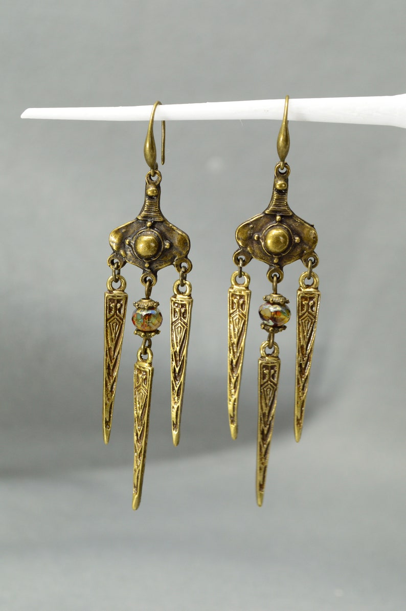 May include: A pair of gold-tone dangle earrings with a geometric design and a single iridescent bead on each earring.