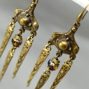 May include: Gold tone dangle earrings with three teardrop-shaped charms and amber-coloured glass beads.
